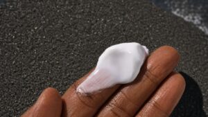 A dollop of white mineral sunscreen on a hand, held over black volcanic sand near the water in Bali